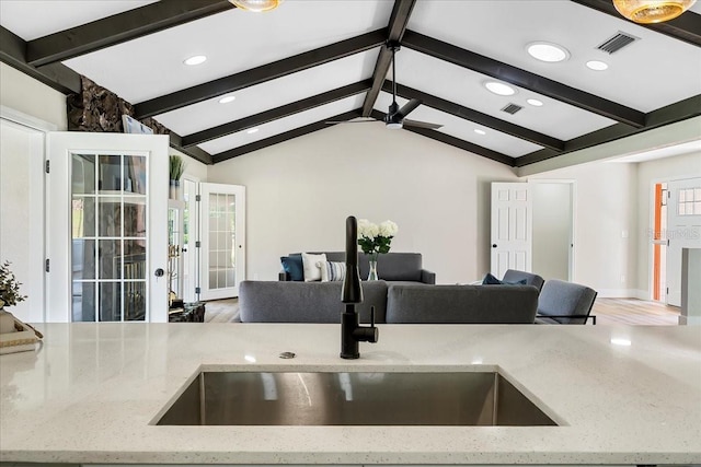 kitchen with light stone counters, visible vents, lofted ceiling with beams, a sink, and open floor plan