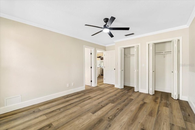 unfurnished bedroom featuring visible vents, two closets, ornamental molding, wood finished floors, and baseboards