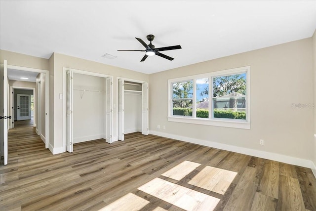 unfurnished bedroom with visible vents, wood finished floors, baseboards, and two closets