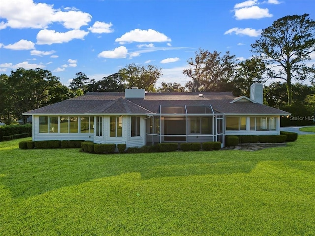 rear view of property with a shingled roof, a lawn, a sunroom, and a chimney