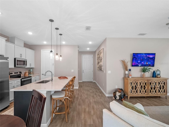 kitchen with visible vents, a breakfast bar, a sink, stainless steel appliances, and light wood-type flooring