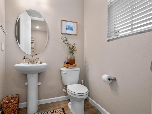 half bathroom with toilet, baseboards, and wood finished floors