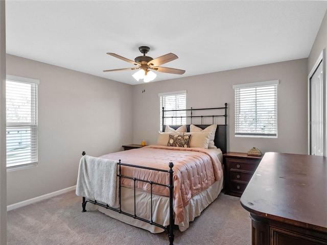 bedroom featuring baseboards, multiple windows, light colored carpet, and ceiling fan