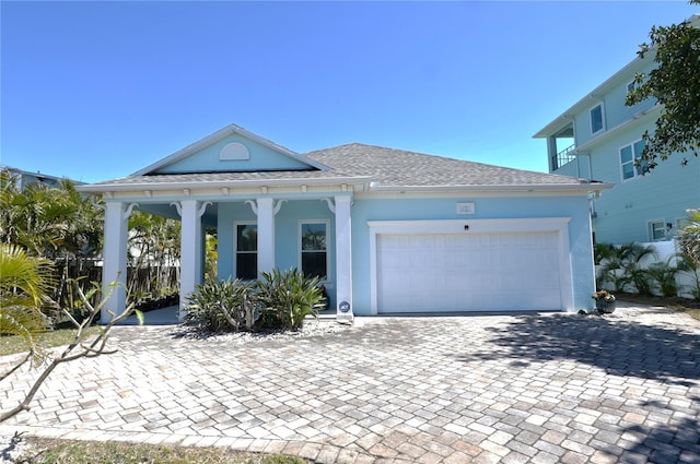 neoclassical home with decorative driveway, an attached garage, roof with shingles, and stucco siding