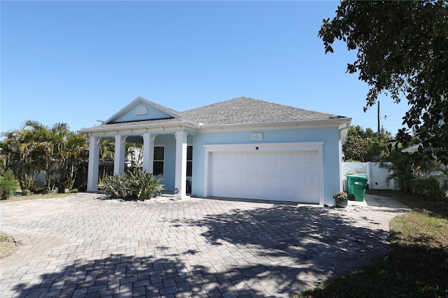 view of front facade with stucco siding, decorative driveway, fence, an attached garage, and a shingled roof