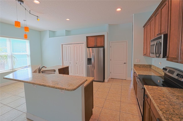 kitchen featuring light tile patterned floors, brown cabinetry, an island with sink, a sink, and appliances with stainless steel finishes