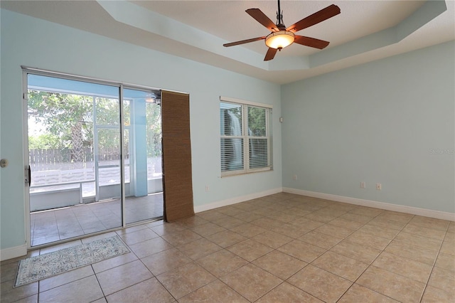 empty room featuring light tile patterned flooring, baseboards, a raised ceiling, and ceiling fan