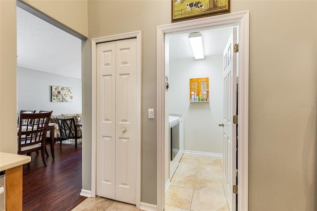 hallway with light tile patterned floors, washing machine and dryer, baseboards, and a textured ceiling