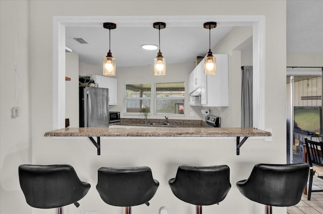 kitchen featuring visible vents, white cabinetry, freestanding refrigerator, and a sink