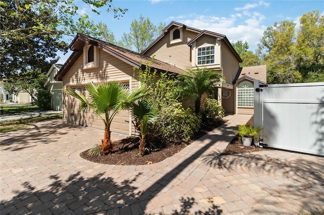 view of front of house featuring decorative driveway, fence, a garage, and roof with shingles