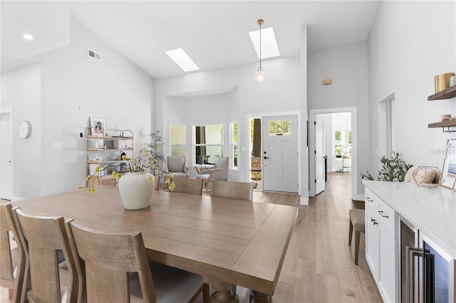 dining room featuring visible vents, high vaulted ceiling, beverage cooler, light wood-style flooring, and a skylight