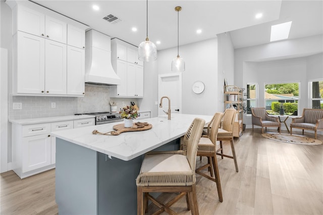 kitchen featuring visible vents, light wood-style flooring, custom range hood, and decorative backsplash