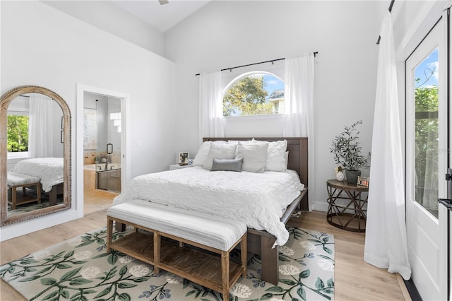 bedroom featuring light wood finished floors, multiple windows, a high ceiling, and connected bathroom