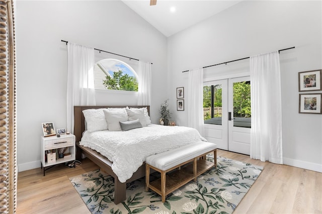 bedroom featuring light wood finished floors, multiple windows, high vaulted ceiling, and baseboards