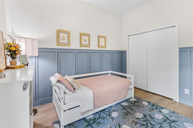 bedroom with a wainscoted wall, a decorative wall, light wood-type flooring, and a closet