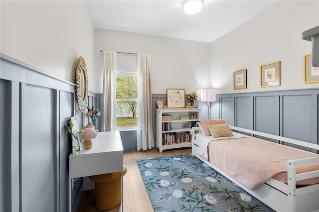 bedroom featuring light wood-style flooring, wainscoting, and a decorative wall