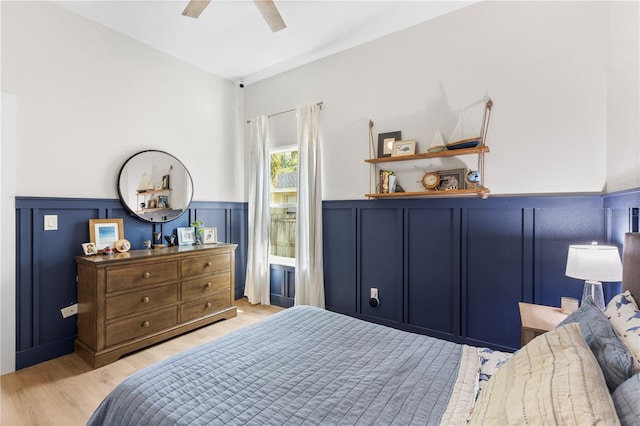 bedroom with connected bathroom, a wainscoted wall, light wood-style floors, a decorative wall, and a ceiling fan