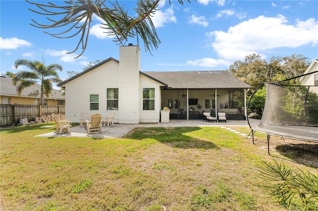 rear view of house with fence, a yard, a chimney, a trampoline, and a patio area