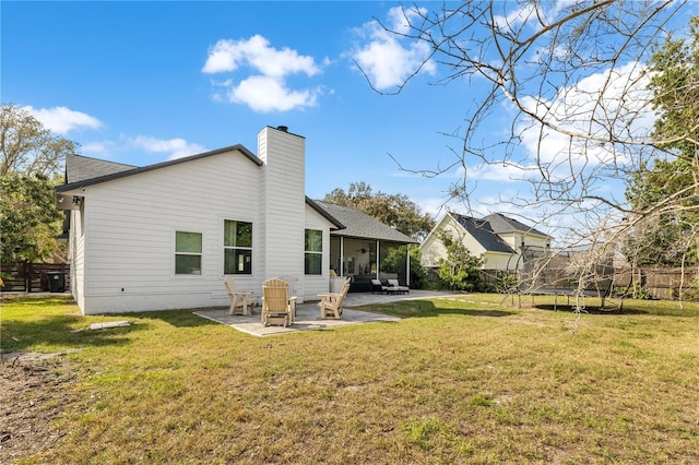 rear view of property featuring fence, a yard, a chimney, a trampoline, and a patio area