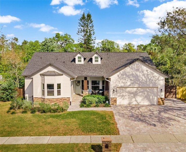 view of front of property featuring a front lawn, decorative driveway, stone siding, an attached garage, and a shingled roof