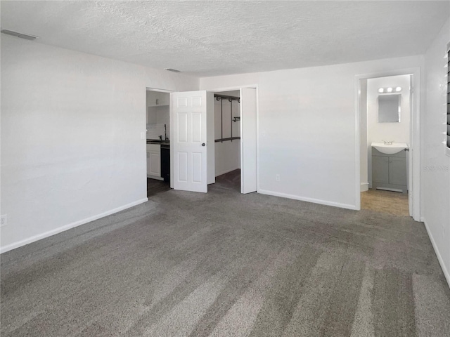 unfurnished bedroom featuring visible vents, a sink, a textured ceiling, carpet flooring, and baseboards