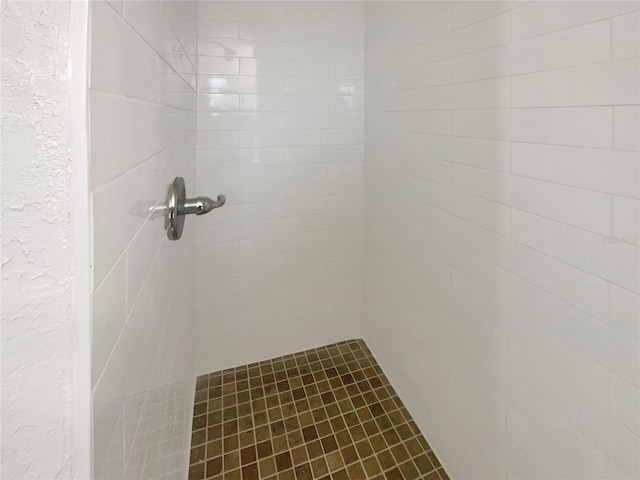 full bathroom featuring a textured wall and a tile shower