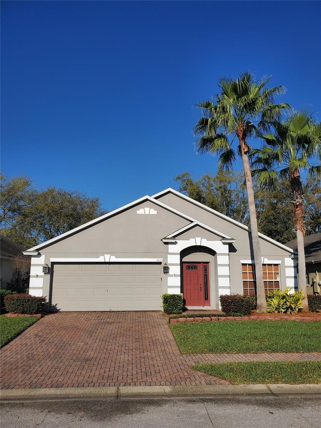 view of front of house with stucco siding, a front yard, decorative driveway, and a garage