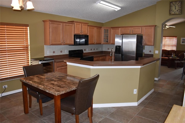 kitchen with dark tile patterned flooring, vaulted ceiling, decorative backsplash, black appliances, and a kitchen island with sink