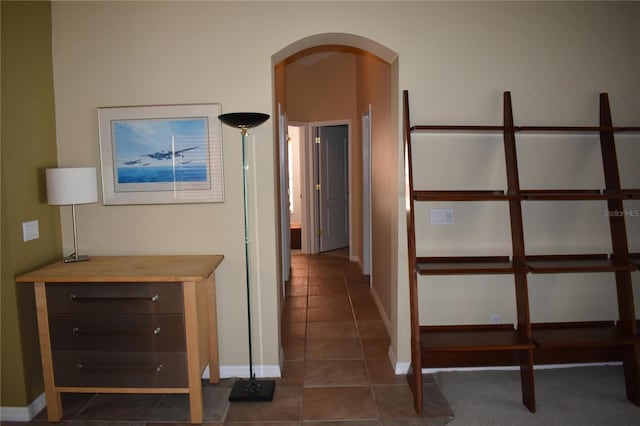 corridor featuring dark tile patterned floors, baseboards, and arched walkways