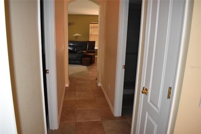 hall featuring tile patterned flooring, arched walkways, and baseboards