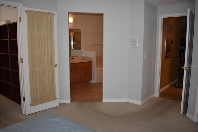 unfurnished bedroom featuring light carpet, connected bathroom, baseboards, and a sink