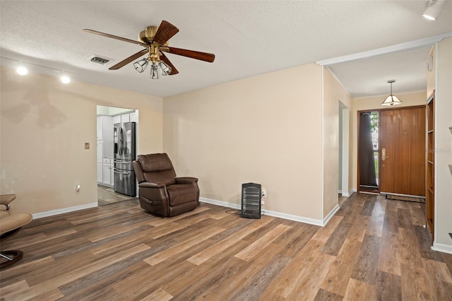 unfurnished room with visible vents, a textured ceiling, wood finished floors, and a ceiling fan