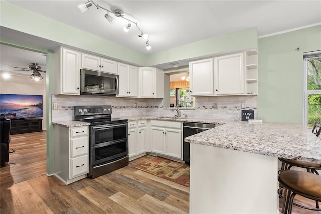 kitchen featuring wood finished floors, appliances with stainless steel finishes, a peninsula, and white cabinetry