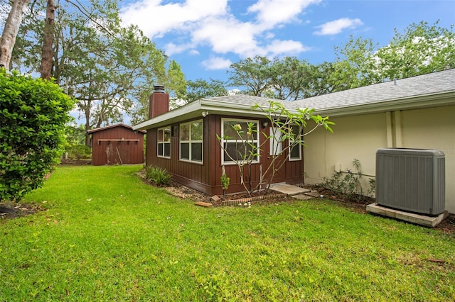 view of property exterior featuring a shingled roof, a lawn, cooling unit, a chimney, and an outdoor structure