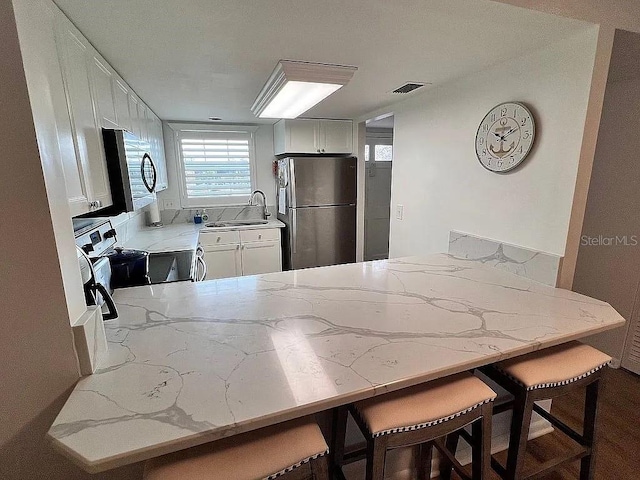 kitchen featuring light stone countertops, visible vents, a peninsula, a sink, and appliances with stainless steel finishes