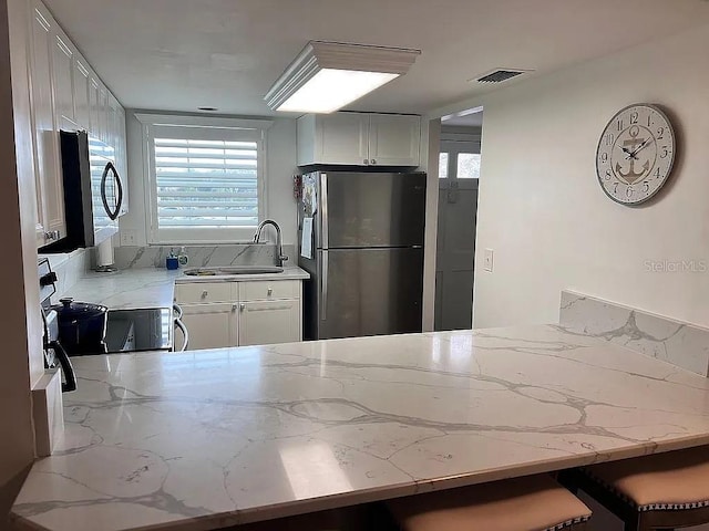 kitchen featuring light stone countertops, visible vents, a peninsula, a sink, and stainless steel appliances