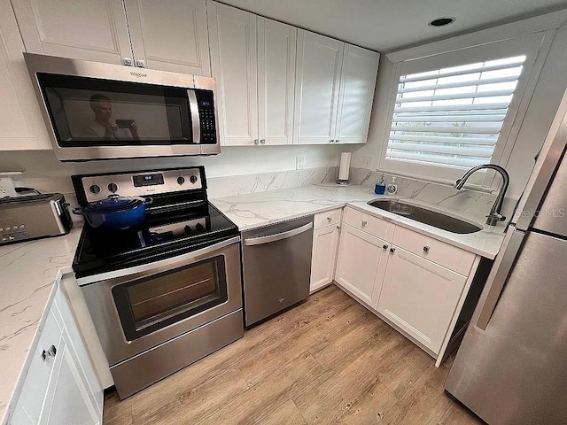 kitchen with light wood-type flooring, a sink, light stone counters, appliances with stainless steel finishes, and white cabinets