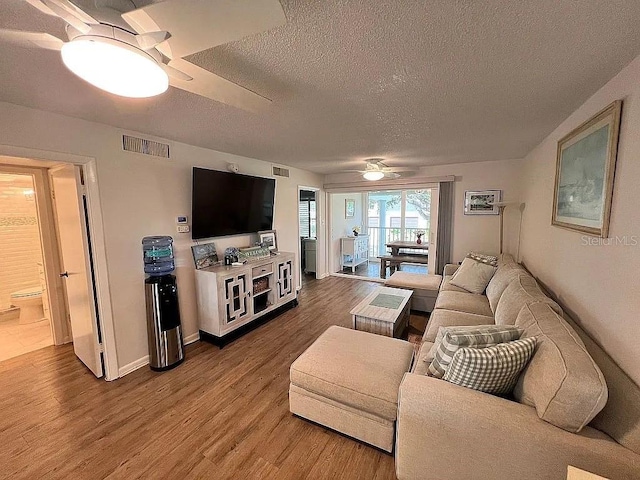 living room with a textured ceiling, wood finished floors, visible vents, and ceiling fan