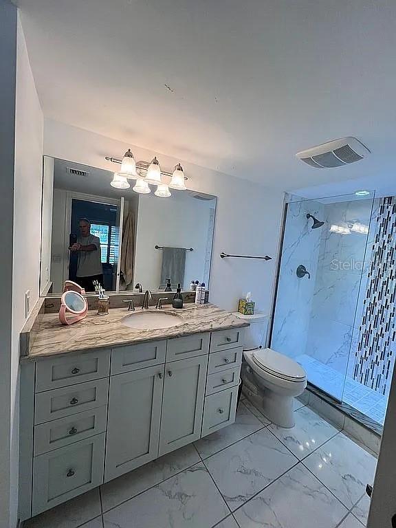 bathroom featuring visible vents, toilet, marble finish floor, walk in shower, and vanity