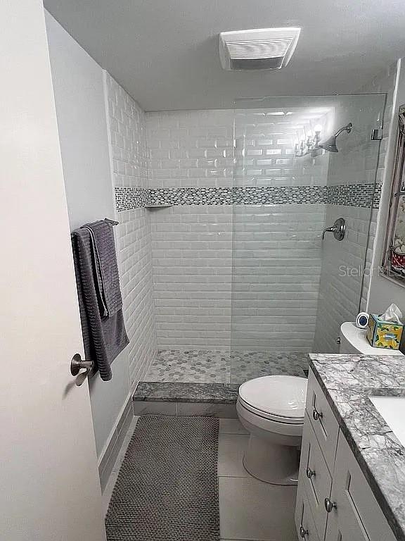 bathroom featuring visible vents, tiled shower, toilet, and vanity