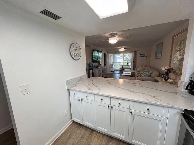 kitchen featuring visible vents, light wood-type flooring, light stone counters, a peninsula, and white cabinets