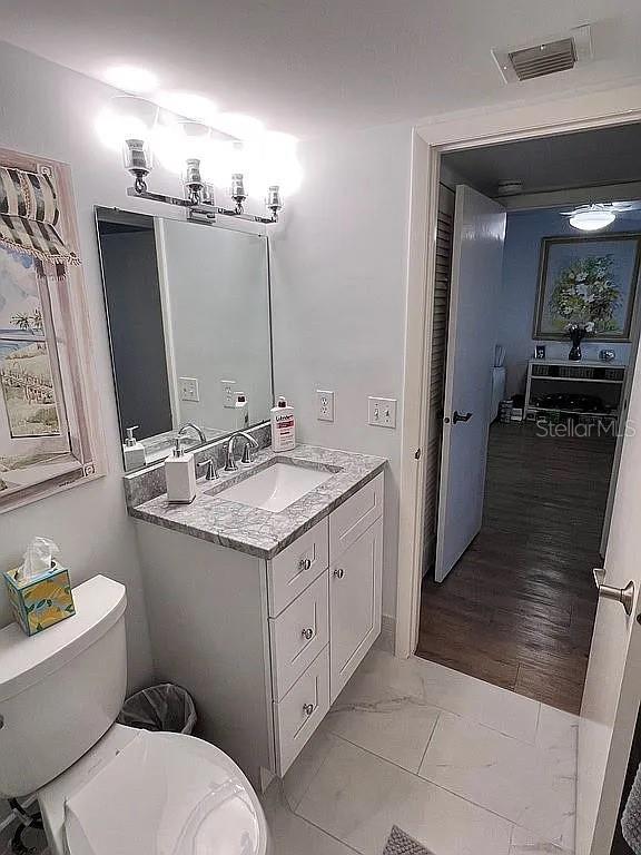 half bath with visible vents, toilet, marble finish floor, and vanity