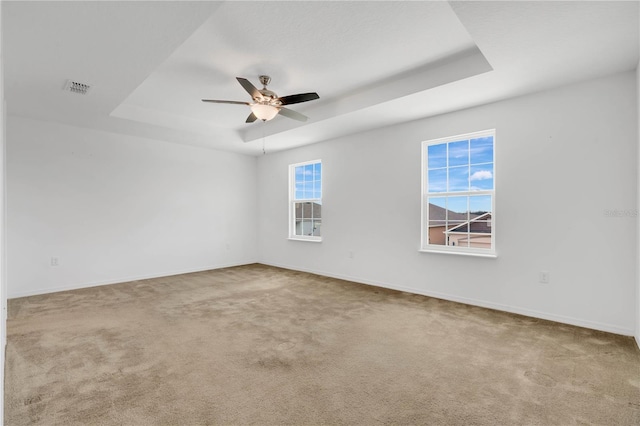 carpeted empty room with a tray ceiling, baseboards, visible vents, and a ceiling fan