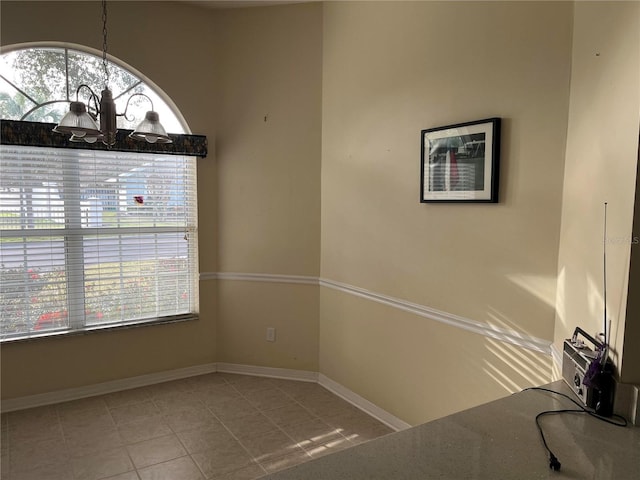 unfurnished dining area with tile patterned flooring, baseboards, a wealth of natural light, and a chandelier