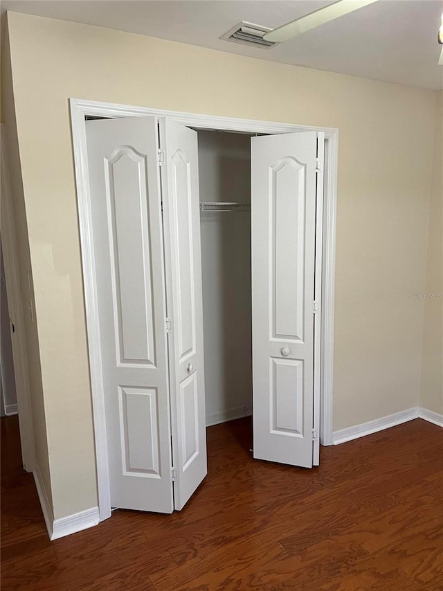 unfurnished bedroom featuring dark wood finished floors, baseboards, visible vents, and a closet