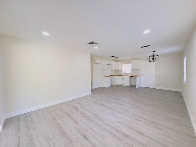 unfurnished living room with baseboards, light wood-type flooring, and a sink