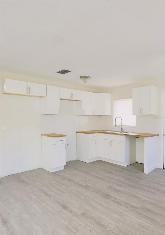 kitchen featuring a sink, visible vents, light wood-style floors, and white cabinetry