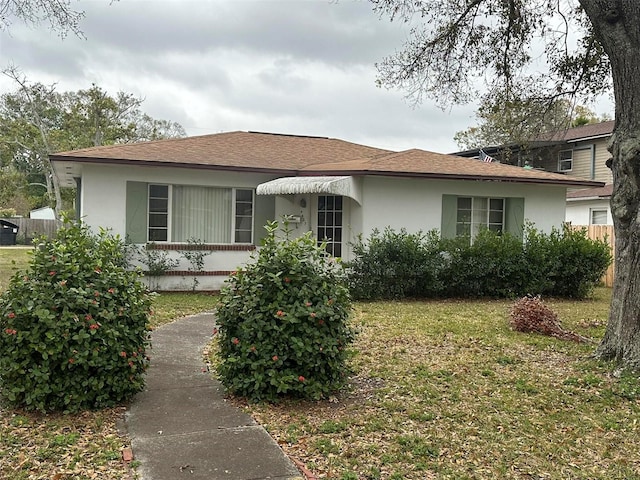 view of front of property featuring stucco siding, a shingled roof, a front lawn, and fence