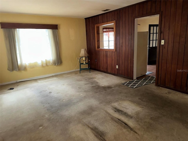 carpeted empty room with visible vents, baseboards, and wooden walls