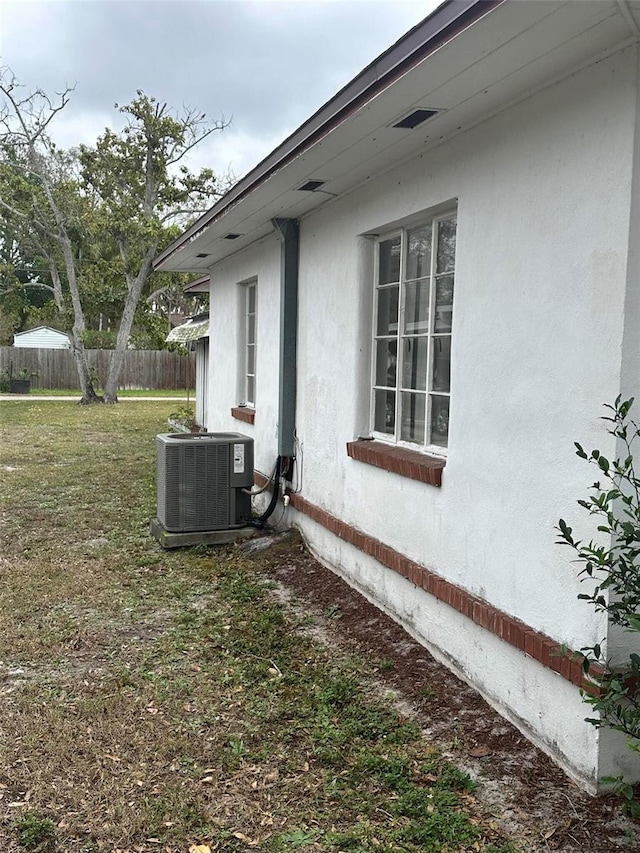 view of side of property with stucco siding, cooling unit, a lawn, and fence